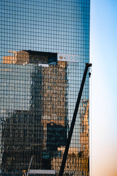A modern glass building reflecting adjacent skyscrapers and construction crane. Architectural lines and urban elements create a dynamic visual effect, capturing the essence of city life and development.