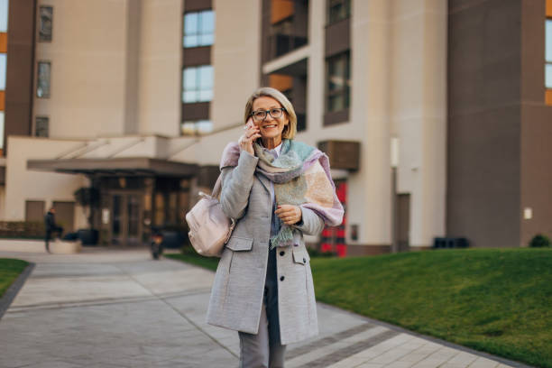 istock Smiling senior woman using smartphone to make a phone call while walking around the city 2174383320