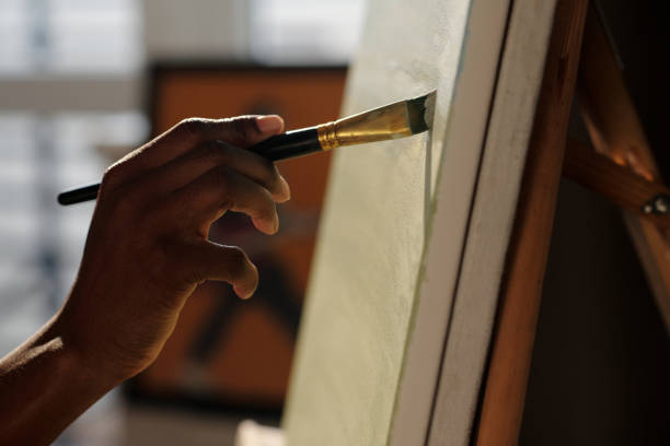 African American Hand Painting on Canvas in Artistic Studio Artistic hand skillfully painting on canvas in an art studio with soft focus on surroundings Creating a beautiful work of art with brushstrokes fine art image pictures stock pictures, royalty-free photos & images