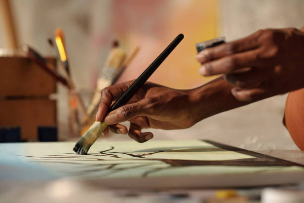 Painter Creating Artwork With Brushes Holding Paint Close-up view of artist's hand holding paintbrush while painting on canvas with brushes and tools around fine art painting stock pictures, royalty-free photos & images