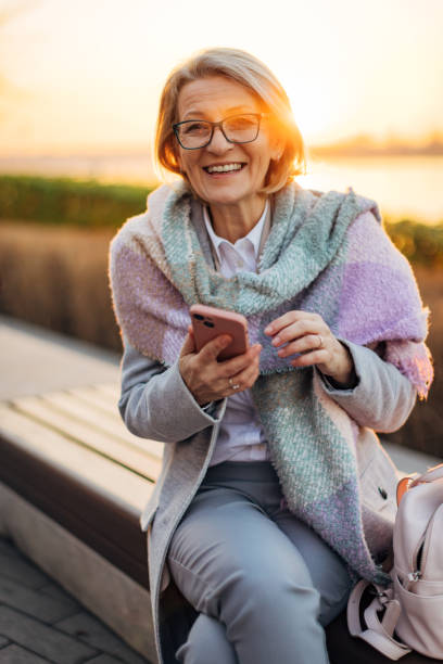 istock Gorgeous senior woman looking directly at the camera while sitting on a park bench overlooking the river during sunset 2174384571