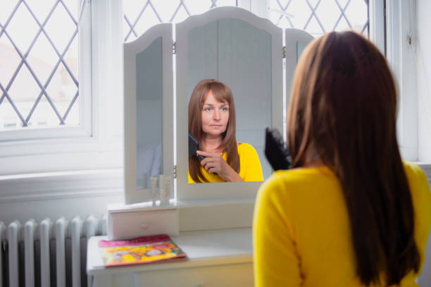 50 year old woman combing her wig in front of a mirror