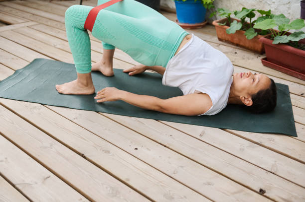 istock Woman practicing yoga on wooden deck, performing bridge pose with resistance band for strength and flexibility 2174394215