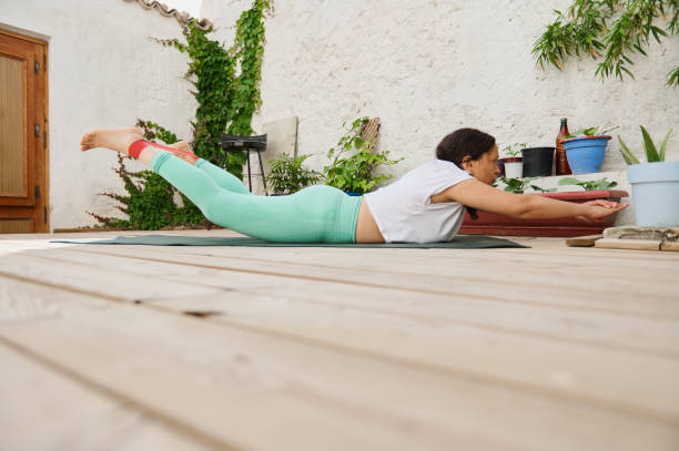 istock Woman practicing yoga outdoors in a backyard performing a locust pose on a wooden deck surrounded by potted plants and green foliage 2174394255