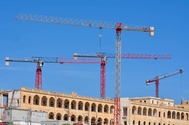 Experience the dynamic contrast between towering red construction cranes and a historic stone building beneath a bright blue sky. This image captures the essence of urban development, where modern technology meets architectural heritage.