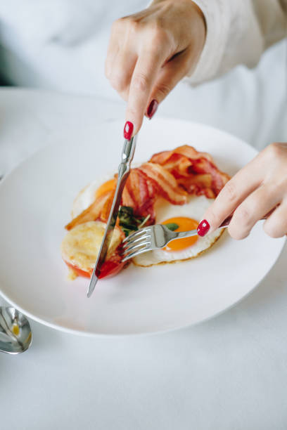 Woman eating breakfast with sunny-side-up egg, bacon, and roasted tomato