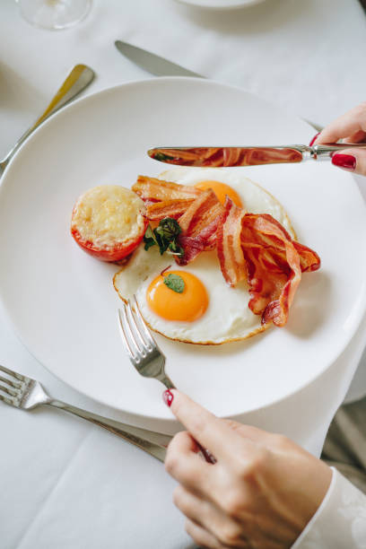 istock Woman eating breakfast with sunny-side-up egg, bacon, and roasted tomato 2174398945