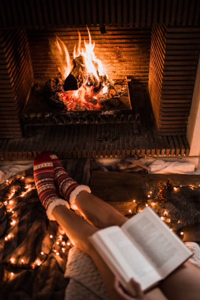 Unrecognizable woman sitting by fireplace and reading book