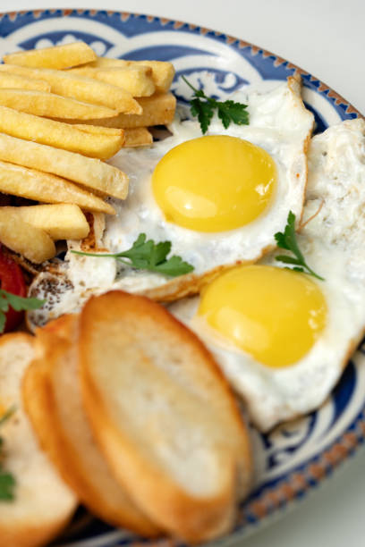 istock Breakfast plate with fried eggs, sausage, tomatoes, and fries served on a decorative blue plate 2174404821