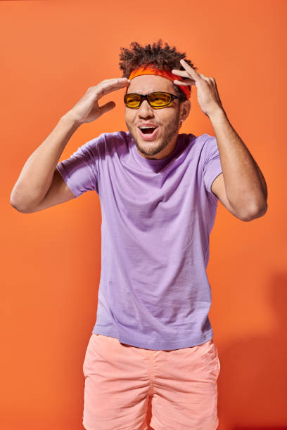 istock A young handsome man exudes joy and excitement against a vibrant orange backdrop in bright attire 2174407652