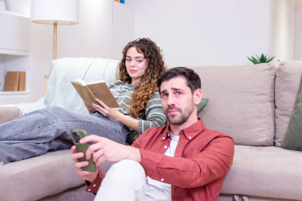 istock Jealous boyfriend watching girlfriend reading book on sofa at home 2174411671