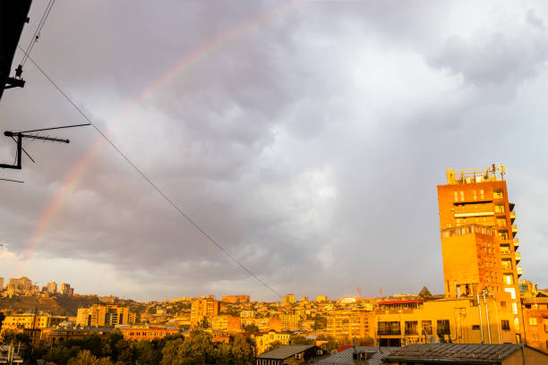 rainbow in gray cloudy sky over residential district in Yerevan city at summer sunset