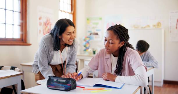 Happy teacher, student and teenager with notebook for question, help or assistance at school. Young, female person or educator with learner for exam, test or studying in classroom for open assessment