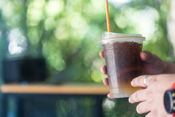Hand holding glass of red soda with straw