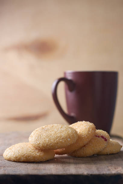 close-up of sugar cookies scattered on wooden table top with cup or mug in background, baked sweet biscuits with crisp texture and buttery flavor, copy space