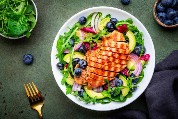 istock Green salad with grilled chicken, avocado and blueberries, rustic background, top view 2174447579
