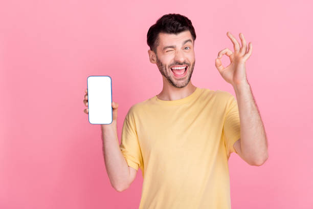 istock Photo of funny guy winking eye hold modern gadget presenting new interface eshop ebank menu okey sign isolated on pink color background 2174451648