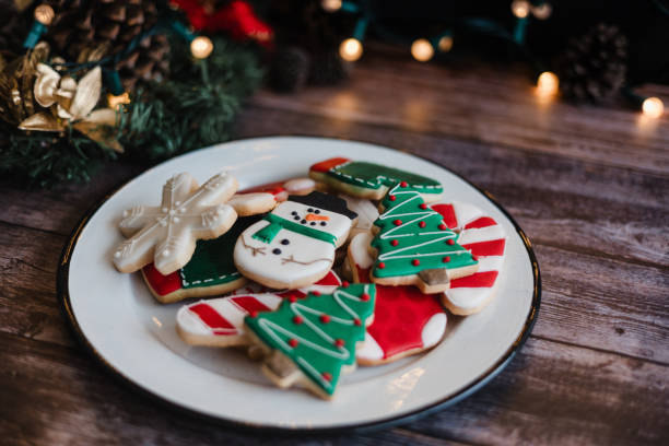 istock Christmas cookies on sheet or plate with golden lights on rustic table. Baking traditional snowman, tree, star cookies and santa hat 2174458128