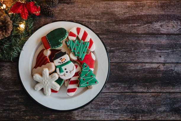 Christmas cookies on sheet or plate with golden lights on rustic table. Baking traditional snowman, tree, star cookies and santa hat stock photo
