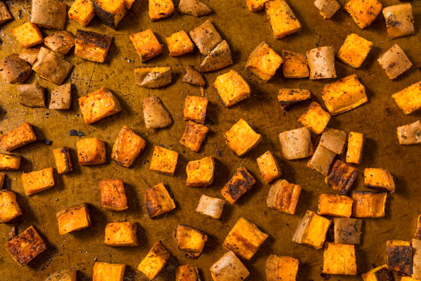 A chef is preparing and chopping root vegetables for roasting in oven in a cozy and warm home kitchen.