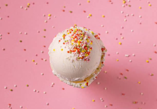 vanilla ice cream scoop decorated with candy sprinkles on pink background, top view