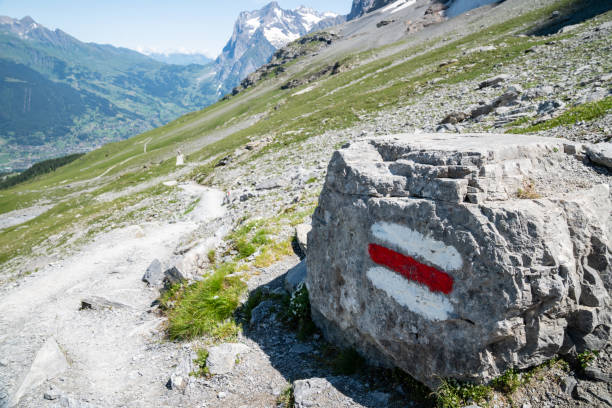 Senior Korean woman hiking a trail from Mannlichen to Kleine Scheidegg with the Eiger in the background of Snowcapped Swiss Alps.