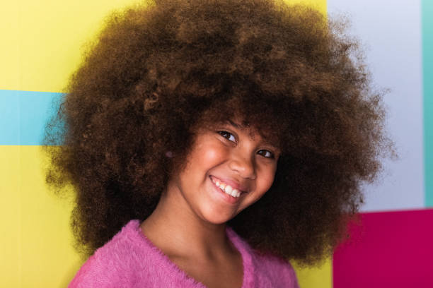 Positive cute black girl with Afro hairstyle looking at camera on colorful background in studio