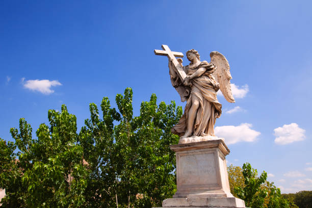 angel statue on the Sant'Angelo Bridge in Rome, featuring a framed view that includes the base, the statue, glimpses of surrounding vegetation, and a backdrop of clear blue sky. The composition offers a harmonious blend of architectural details, natural elements, and celestial beauty