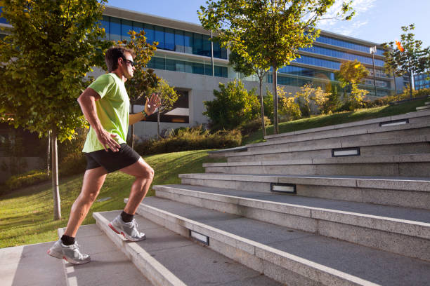 Businessman in green shirt and trousers walking down wide outdoor stairs carrying bag in hand. Clear day with sunlight illuminating stairs and railings in background