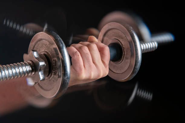 Close up of man's hand exercising with heavy dumbbell with motion effect against black background