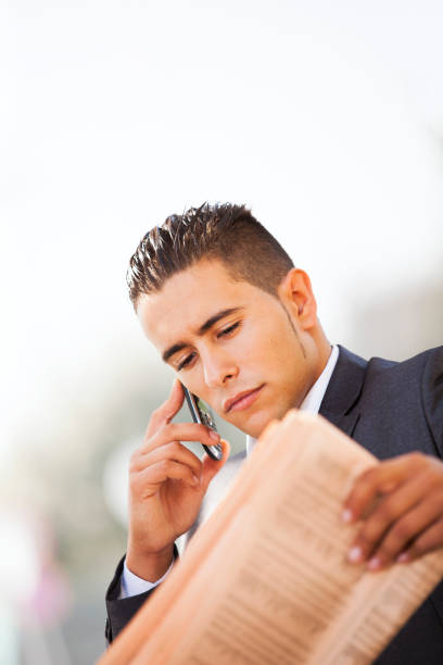 Horizontal color image of a young man reading newspaper. Low angle view.