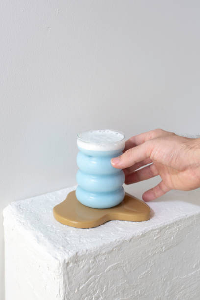 Hand Placing Blue Foamy Drink On Beige Wooden Coaster.