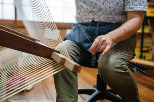 Senior woman preparing a large spool of thread for weaving a kimono fabric on a wooden loom