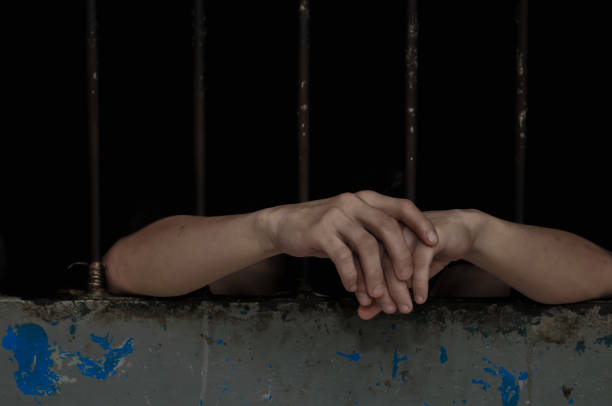 istock hands of a prisoner behind prison bars on black background 2174546565