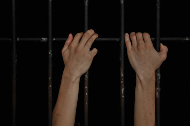 istock hands of a prisoner behind prison bars on black background 2174546569