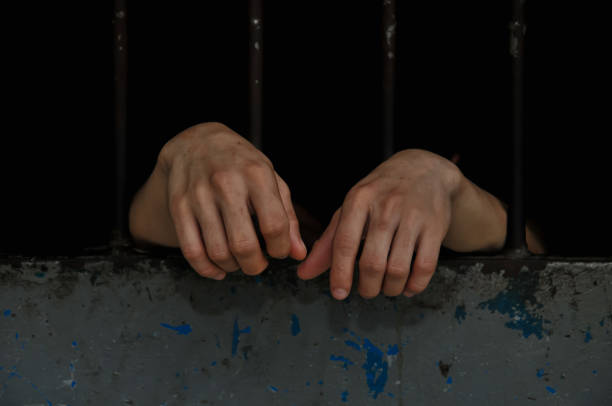 istock hands of a prisoner behind prison bars on black background 2174546585