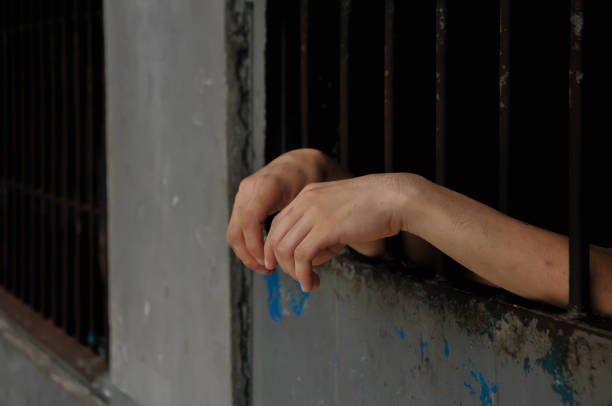 istock hands of a prisoner behind prison bars on black background 2174546624