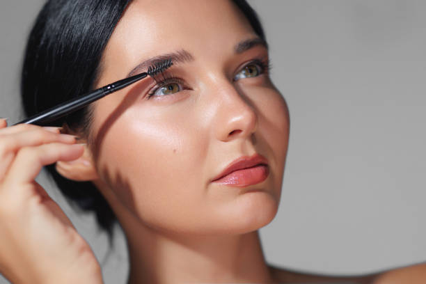 istock Woman Applying Makeup to Eyebrows With Brush in Soft Lighting 2174548750
