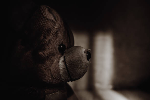 A shabby and ugly teddy bear in a dark room