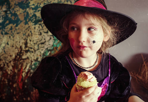 istock Savoring Halloween sweets. Young blonde in witch costume enjoys cupcake 2174567885