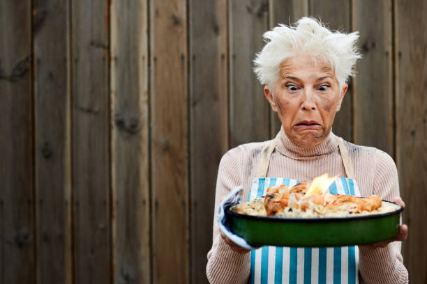 Bizarre senior woman feeling displeased after her dinner is burning in a tray. Copy space.