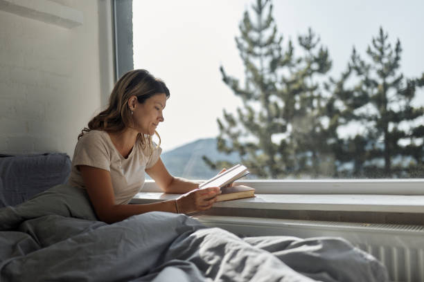 istock Relaxed woman reading a book in bed by the window. 2174572584