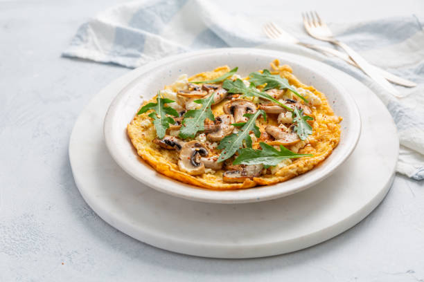 istock Homemade egg omelet with champignons and arugula and herbs on white kitchen table 2174580229