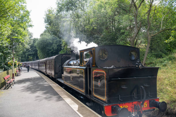 09.08.2024 Haworth, UK. A classic steam train emits gentle puffs of smoke as it prepares to leave the quaint Haworth Station. Passengers and visitors line the platform, enjoying the nostalgic ambiance of this historic locomotive.