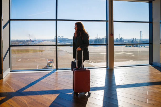 istock Young woman standing at the gate with wheeled suitcase 2174584463