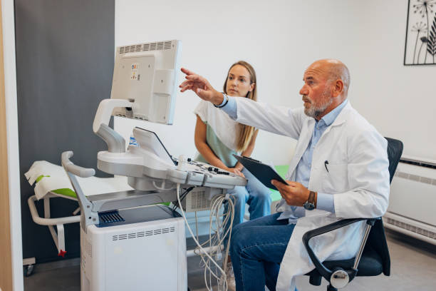 A senior doctor points to a computer monitor with CT scans while explaining test results to a female patient seated beside him