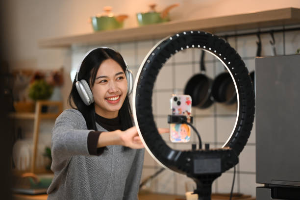 istock Joyful young woman dancing in her kitchen while recording herself with smartphone mounted on a ring light 2174602140