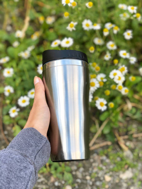 istock Hand holding thermos with chamomile flowers in the background 2174602147