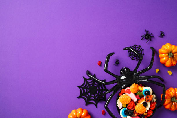 istock Festive Halloween candy spread with spider decor on purple background. Flat lay, top view. 2174606771