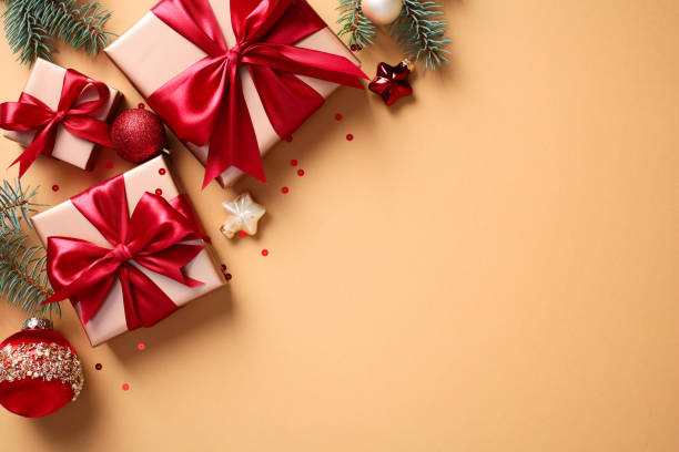 istock Christmas gift boxes with vibrant red bows, Christmas ornaments, and pine branches on a warm beige backdrop 2174607886